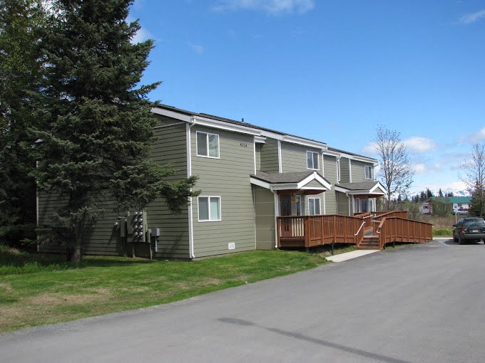 a green house with a wooden deck on the side of a street at Conifer Woods Apartments, Homer, Alaska