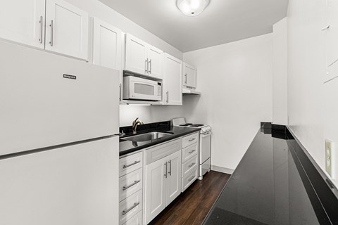 A kitchen with white cabinets and black countertops.