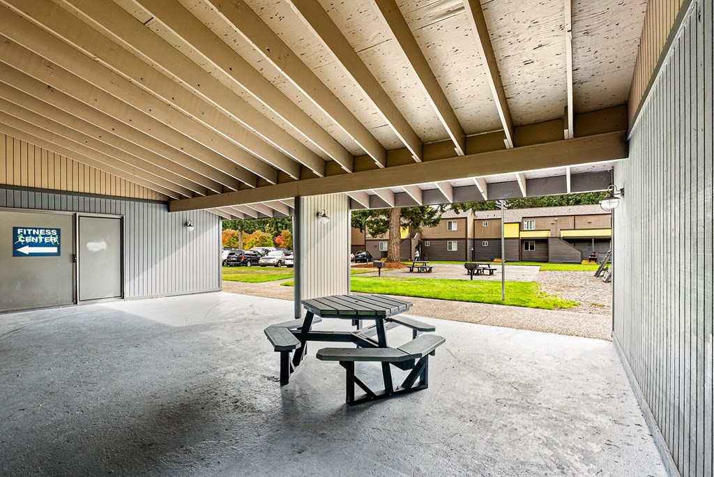 A picnic table sits under a covered patio area.