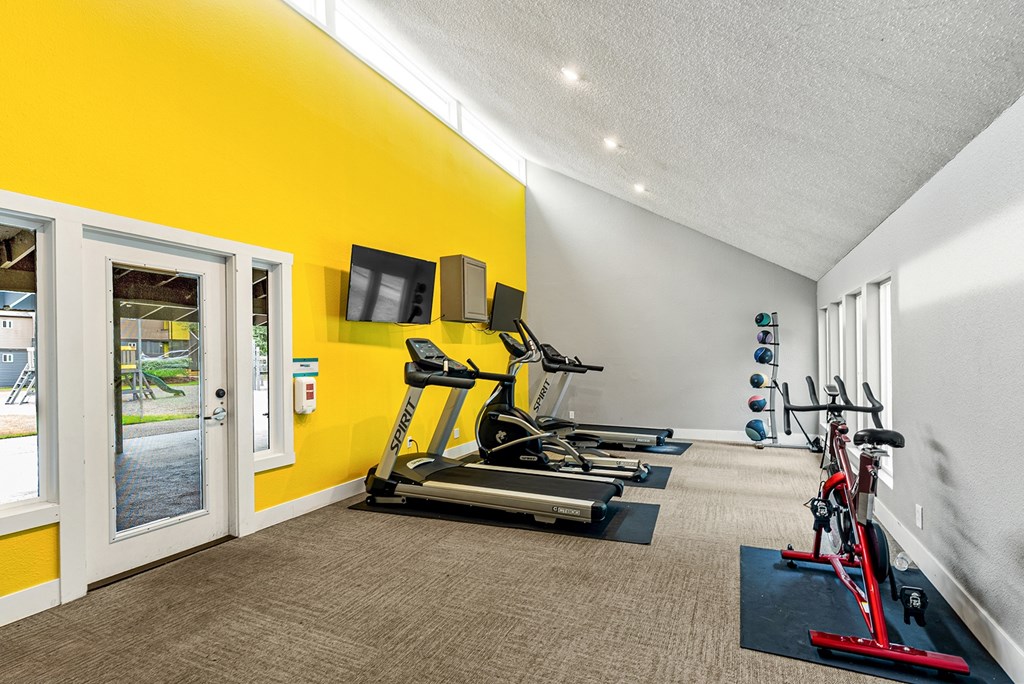 A bright yellow wall with a treadmill and exercise equipment in a room.