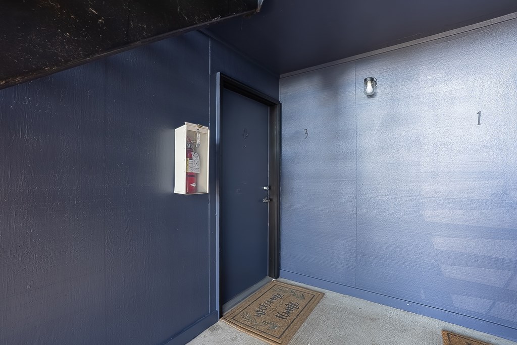 A blue wall with a door and a mat on the floor.