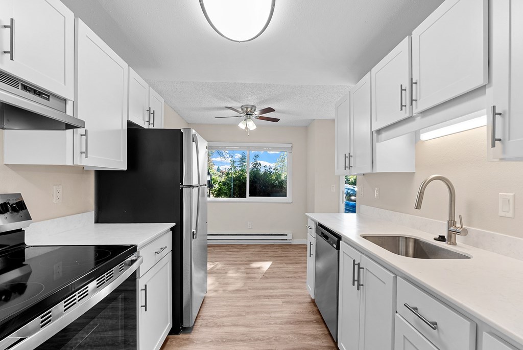 A kitchen with white cabinets, refrigerator and a window