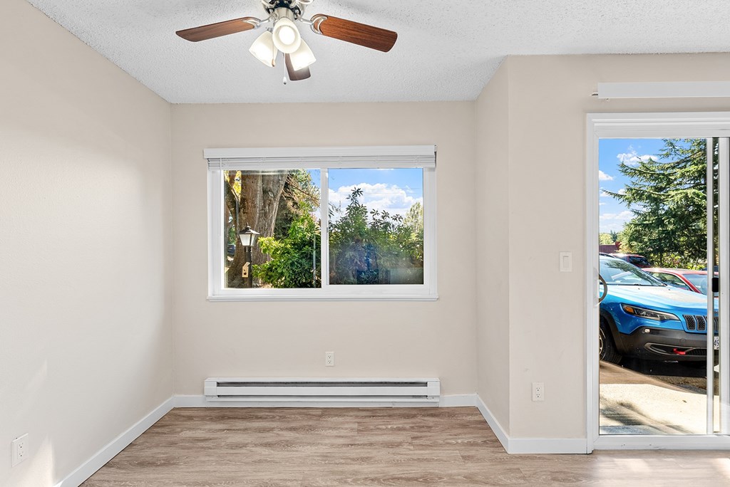 A room with a ceiling fan, wooden floors and windows