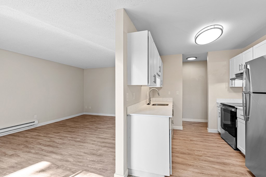 A kitchen with white cabinets and a refrigerator with a view of the living room