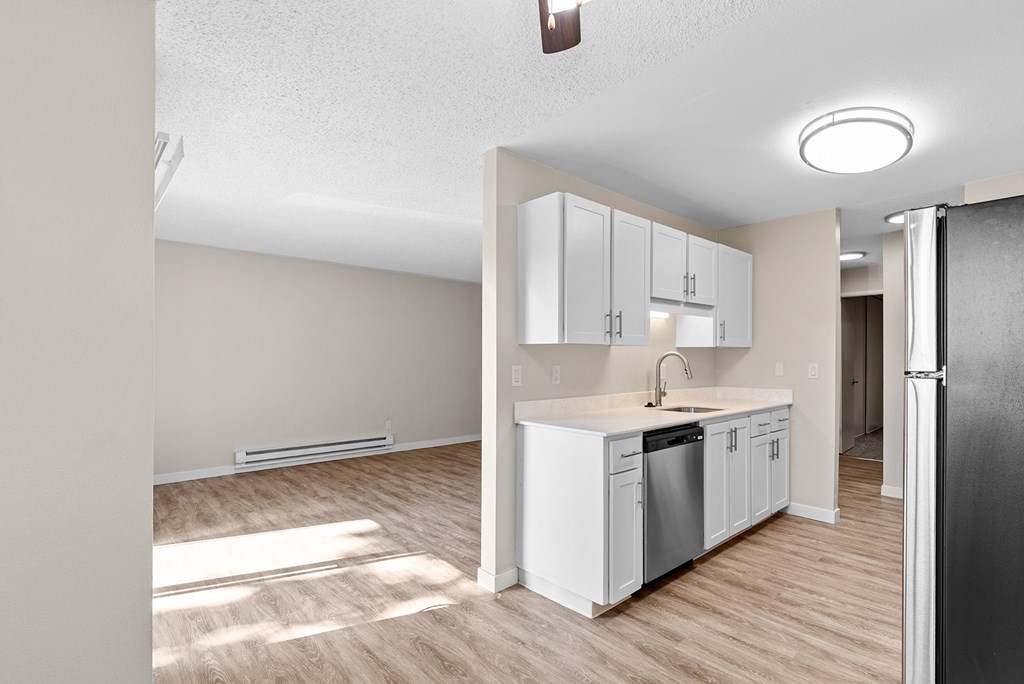 A kitchen with white cabinets and a black refrigerator and a view of the living room