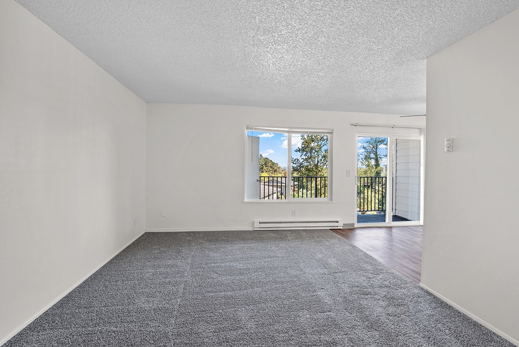 Livingroom with a carpeted floor and a window overlooking a balcony.