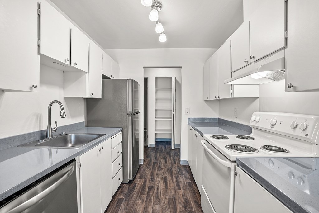 A kitchen with white appliances and cabinets and wooden floors.