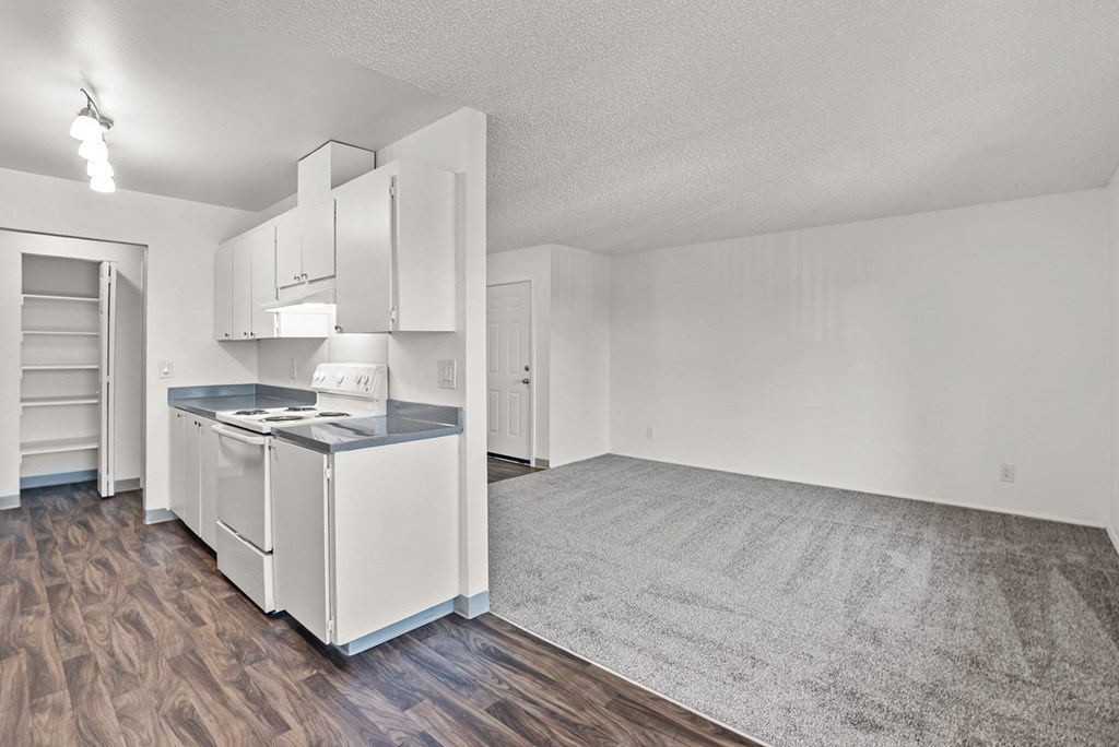 Kitchen with white appliances and wooden floors and a view of the living room