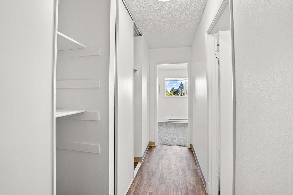 A long hallway with white walls, wood floors, and storage