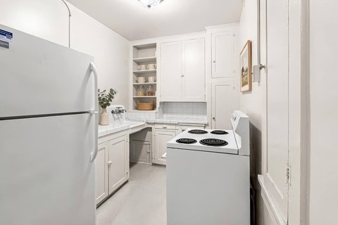 A white kitchen with a refrigerator, stove, and cabinets.