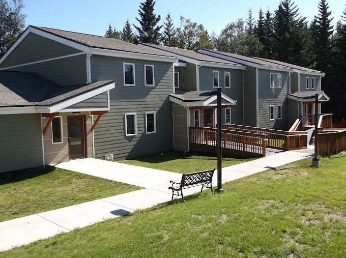 a row of houses with a yard and a bench at Conifer Woods Apartments, Homer