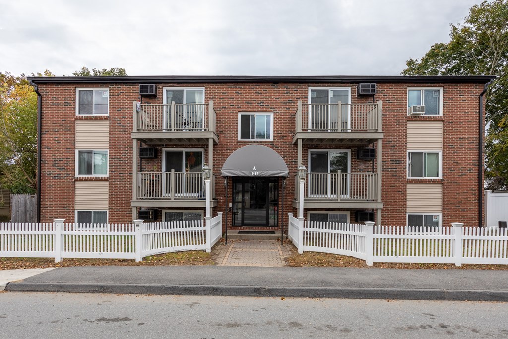 the front of a brick apartment building with a white fence at Flats at Merrill Pond, Massachusetts