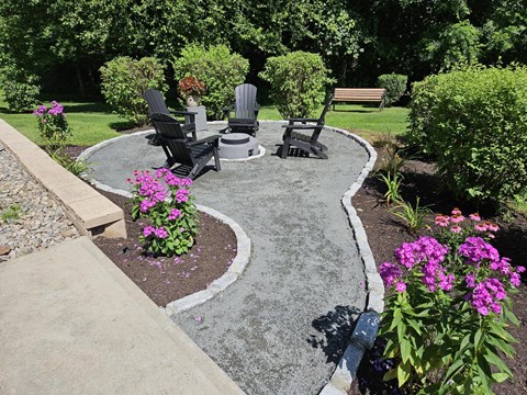 A garden with a circular concrete table surrounded by chairs and flowers.
