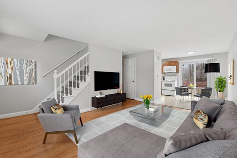 A living room with a grey couch, a grey armchair, a glass coffee table and a television.