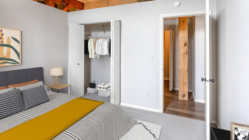 A bedroom with a bed, a nightstand, a lamp, a rug, a picture, a wardrobe, and a door.