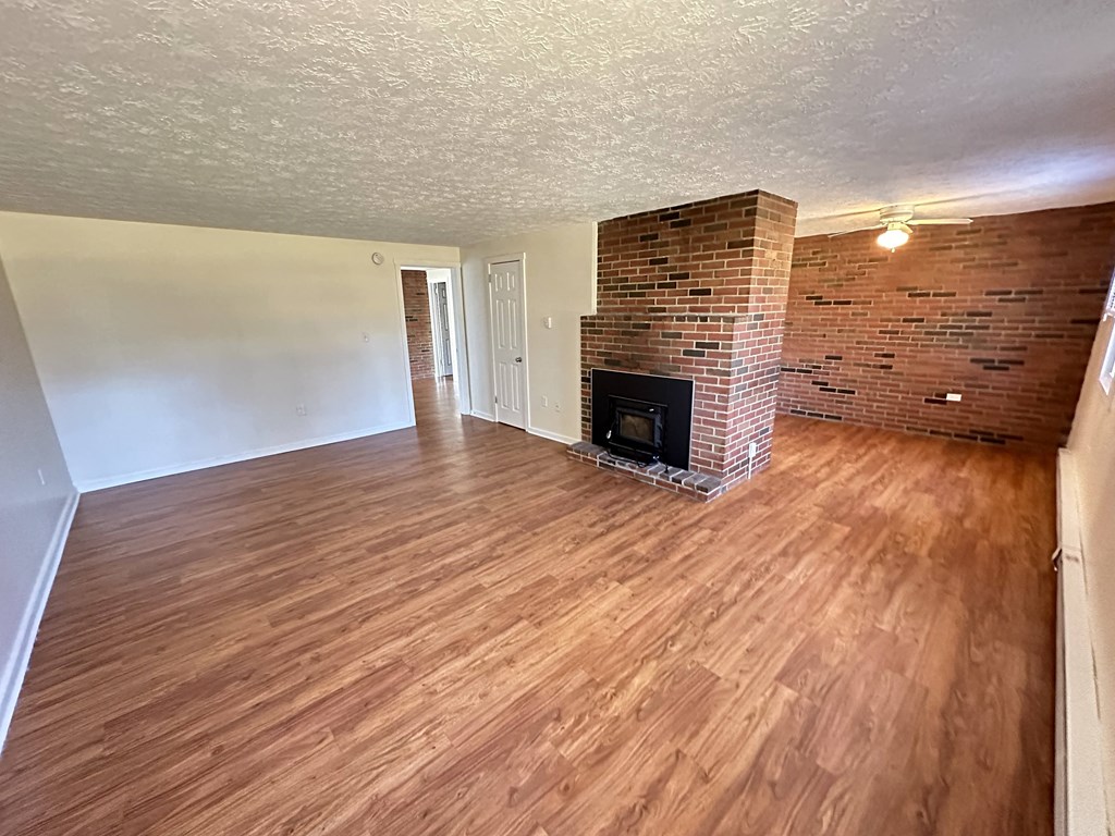 an empty living room with a brick fireplace and wooden floors