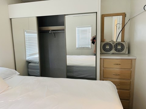 A bedroom with a white bed, a wooden dresser, and a mirror.