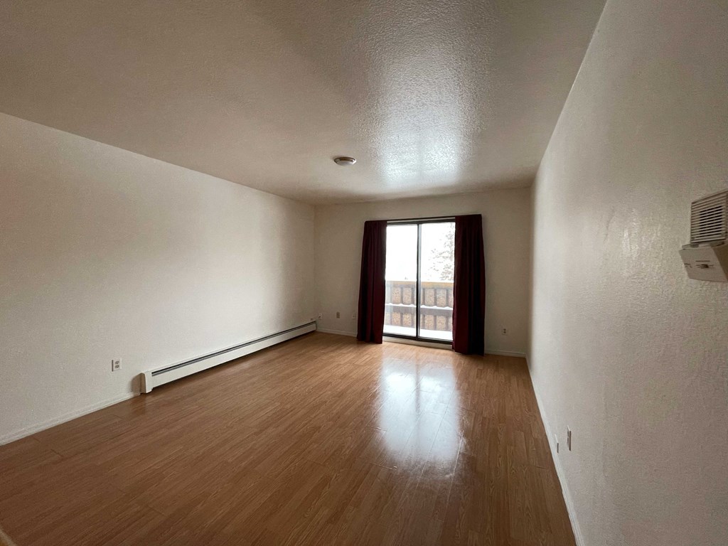 an empty living room with wood floors and a door to a balcony