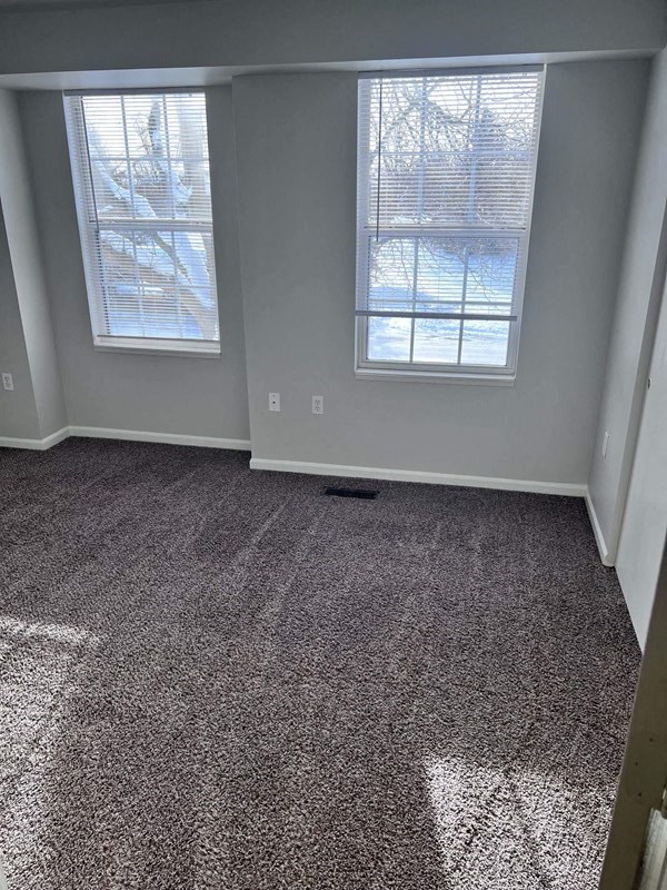an empty room with a carpeted floor and two windows