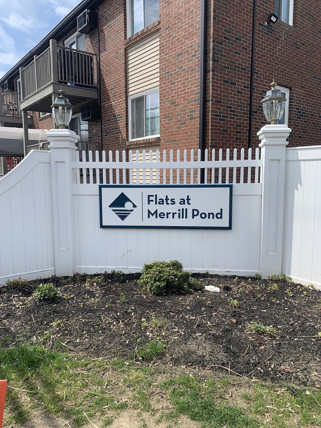 a white fence with a sign that reads Flats at Flats at Merrill Pond, Worcester, MA 01607