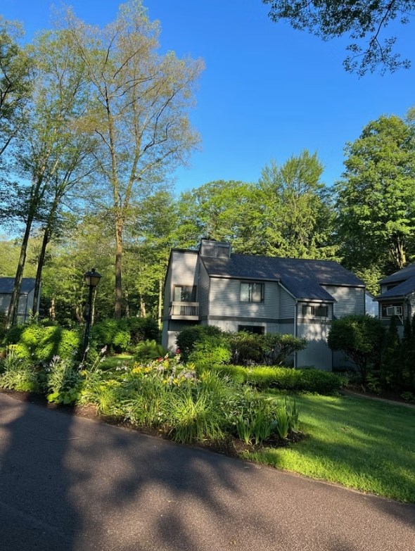 A house with a grey roof and white walls is surrounded by greenery and trees.