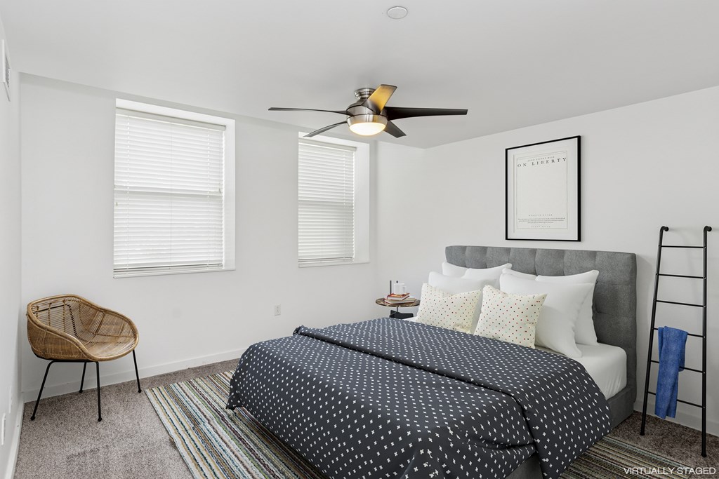 A bedroom with a bed, chair, and a ceiling fan.