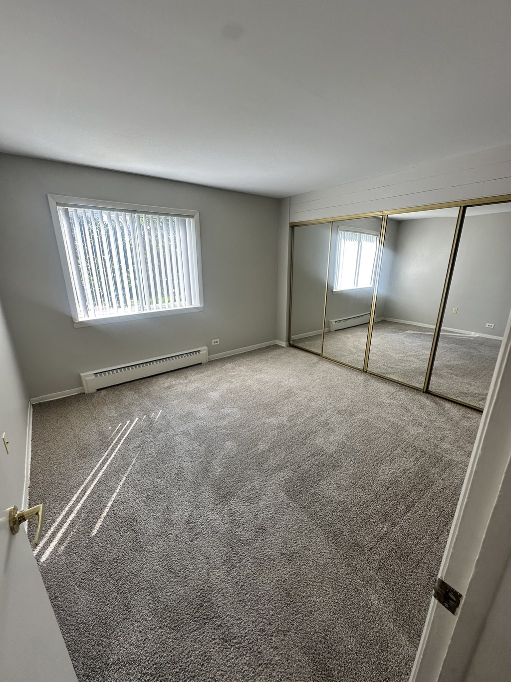 a room with a carpeted floor and a window and a mirrored closet at River Oaks, North Aurora, IL