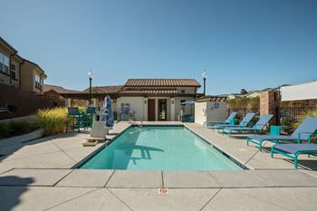 a swimming pool with blue chairs and a house in the background