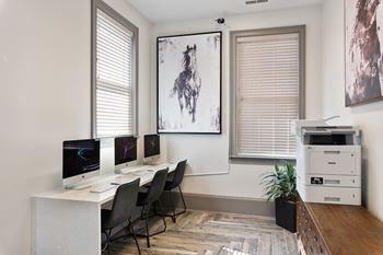 an office with three computer monitors on a desk and a painting on the wall