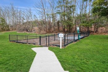 a fenced in dog park with green grass and trees
