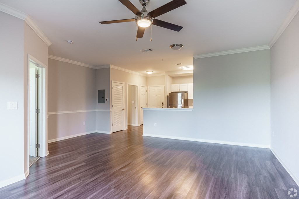 an empty living room with a ceiling fan and a kitchen