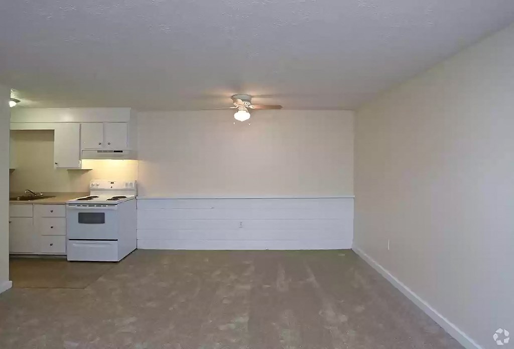 an empty living room with a ceiling fan and a kitchen
