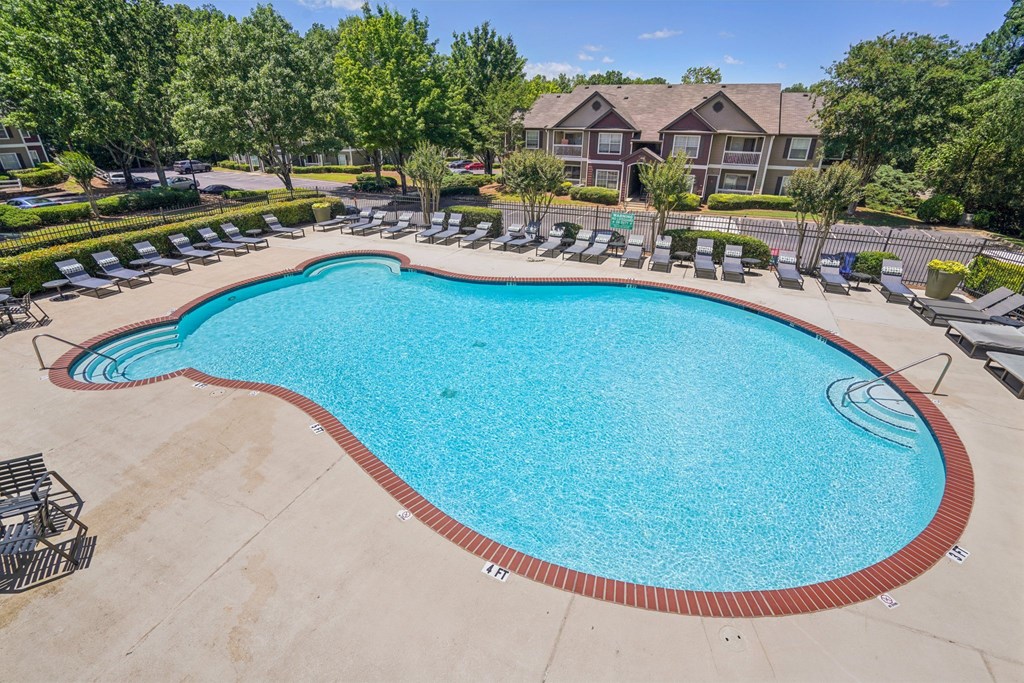 A large outdoor swimming pool surrounded by lounge chairs and trees.