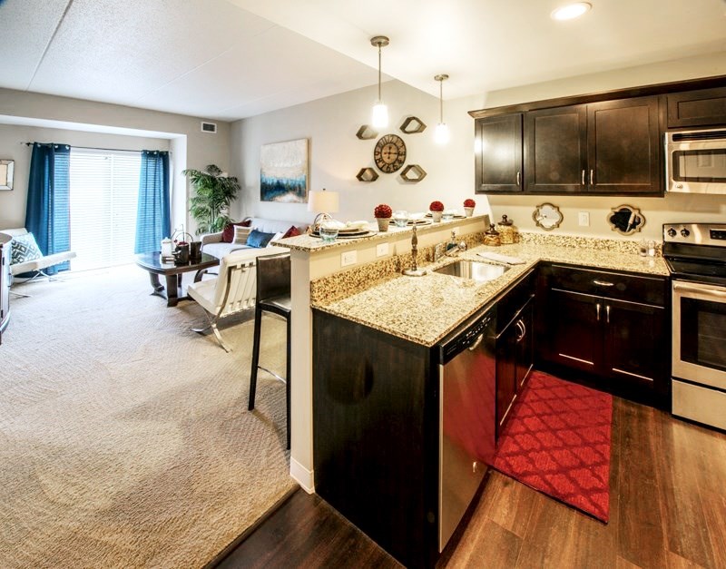 A kitchen with dark cabinets and view of the living room