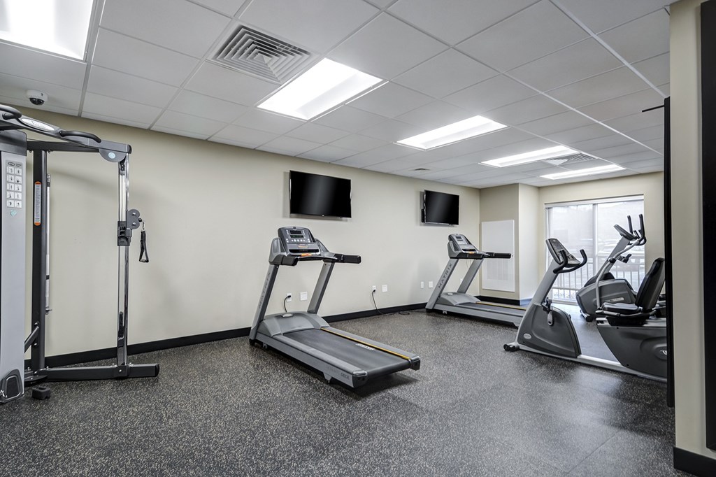 A gym with treadmills, elliptical machines, and a television.