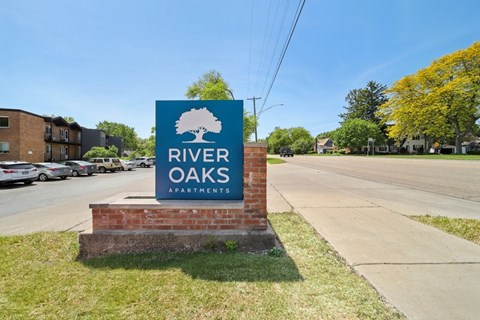 A sign for River Oaks Apartments is displayed in front of a parking lot.