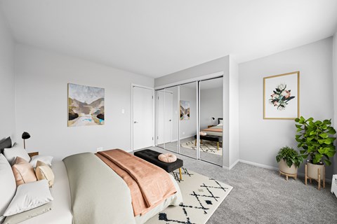 A bedroom with a bed, a couch, a rug, and a plant.