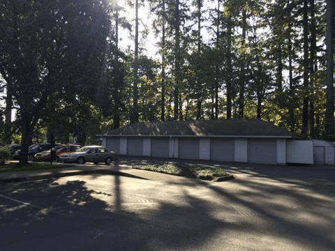 A parking lot with a white building and trees in the background.