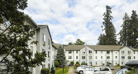 A white building with a flag on top is surrounded by trees and cars.