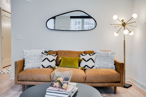 A living room with a brown couch and a round mirror on the wall.