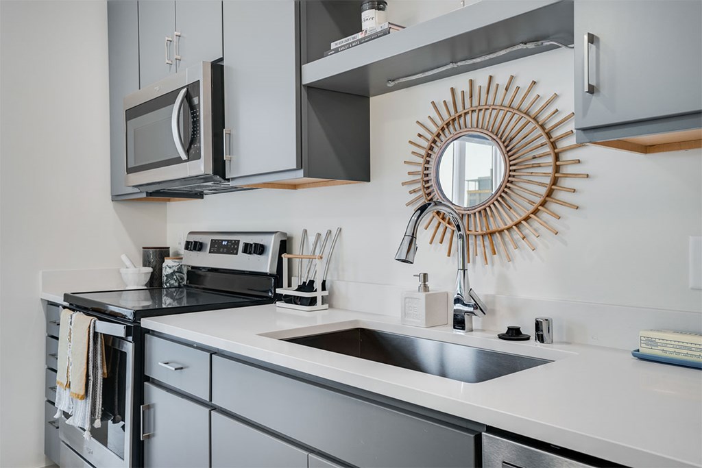 A modern kitchen with a stove, microwave, and a large mirror on the wall at Sora Apartments, Minneapolis, MN
