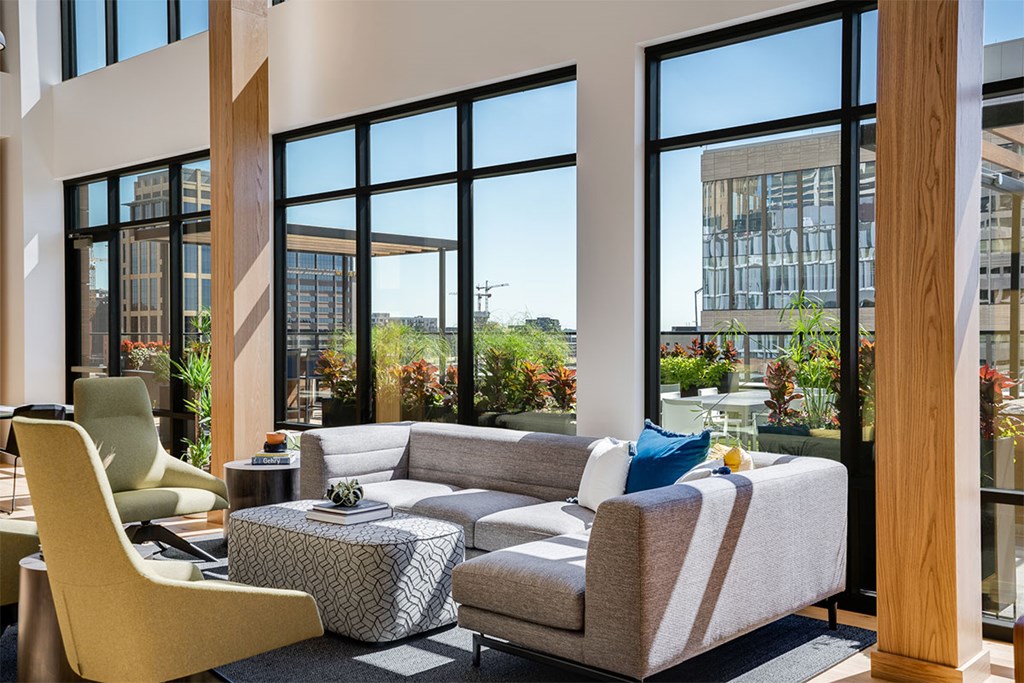 Front lounge with a yellow chair and a grey couch and large windows in the background at Sora Apartments, Minneapolis, MN