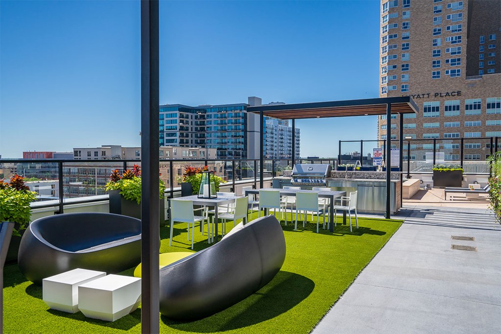 A modern outdoor seating area with a curved bench and a table with chairs. at Sora Apartments, Minneapolis