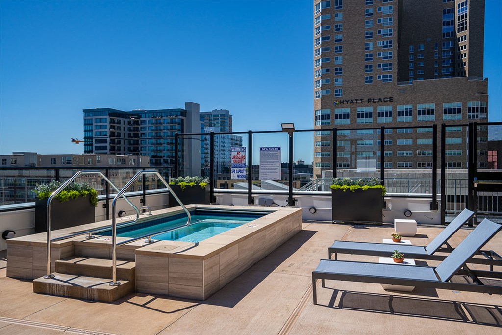 A pool on a rooftop with lounge chairs and a building in the background at Sora Apartments, Minnesota