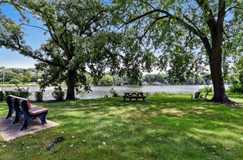 a park with benches and a picnic table near a river at The View Apartments St Charles, St Charles, IL