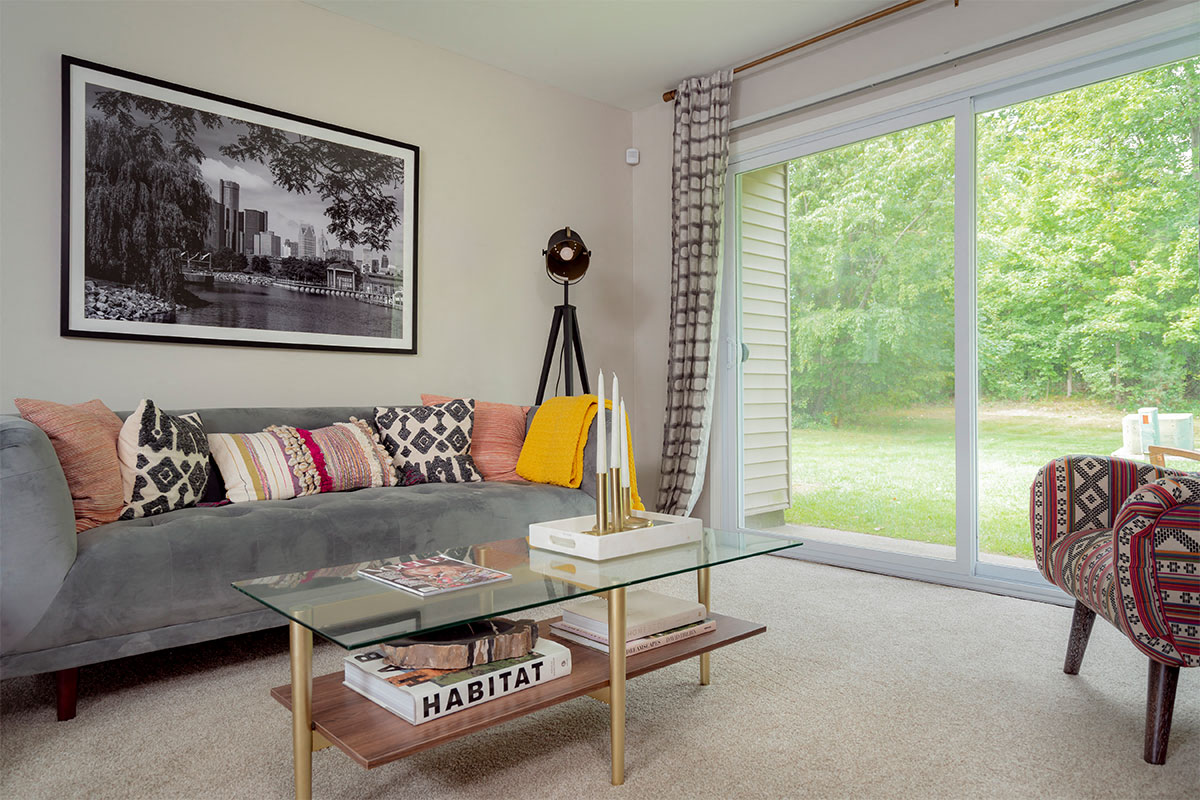 A living room with a grey couch, a glass coffee table, and a chair with a patterned cushion.