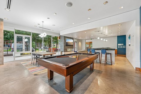 A pool table is in the middle of a room with a bar and a television.