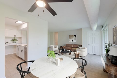 An eating area with a white table and chairs, view of the kitchen and living room