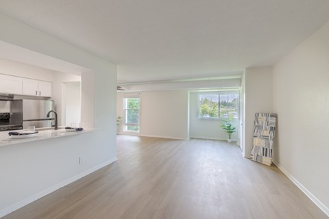 A spacious, empty room with a kitchen area to the left and a doorway leading to another room.