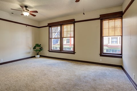 an empty living room with two windows and a ceiling fan